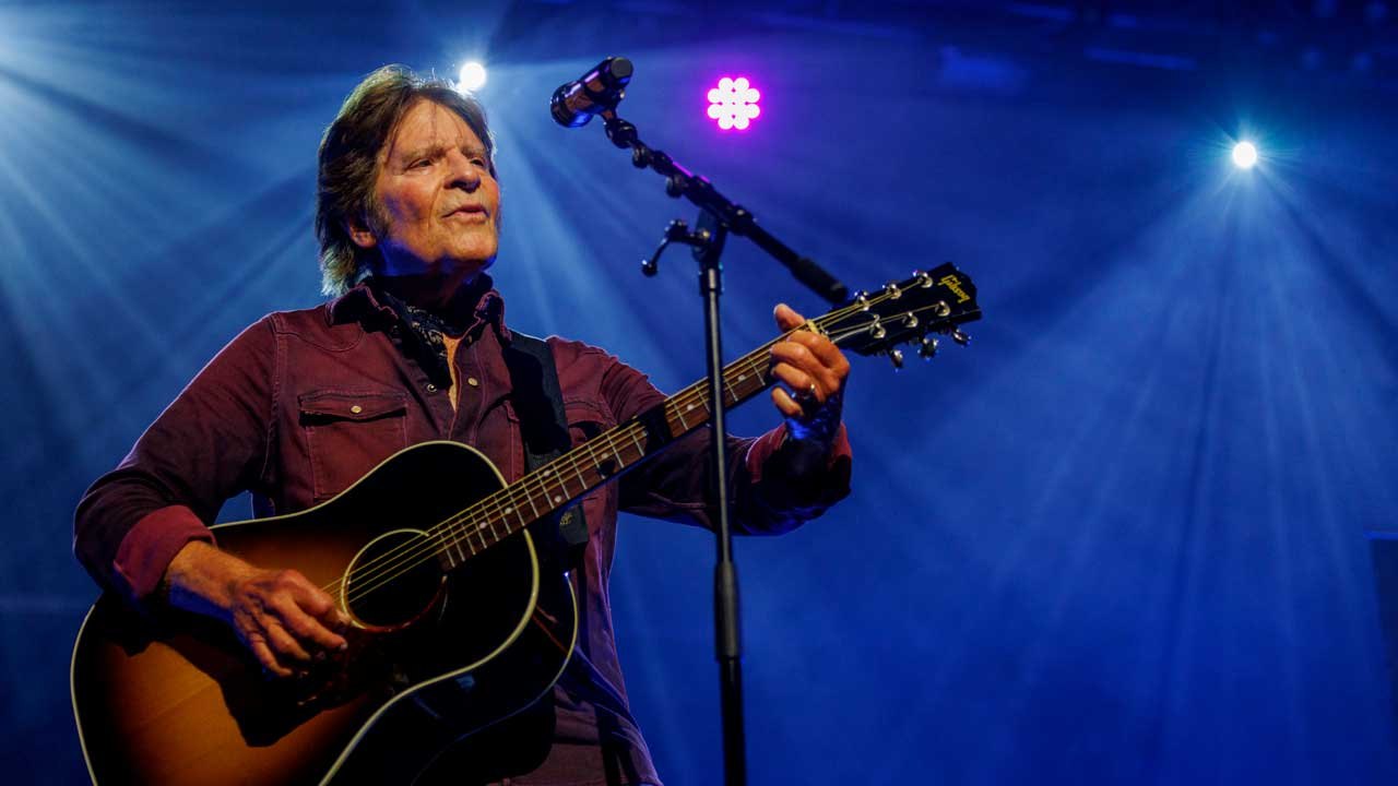 Singer playing an acoustic guitar at a microphone on a blue-lit stage